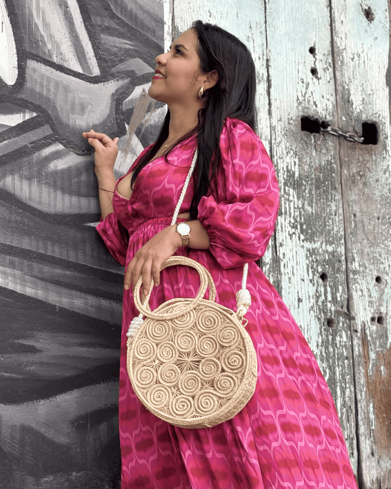 Mujer de perfil con un bolso redondo y azas con lazo blanco elaborado en palma de iraca