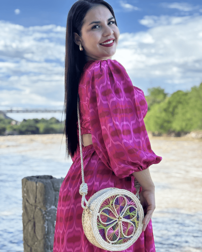 Mujer de perfil con un bolso tipo yoyo colorido y lazo beige elaborado en palma de iraca